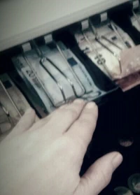 Person die Geld aus einer Kasse nimmt als Synonym für Diebstahl.